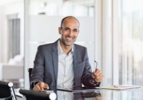 Happy mature business man holding spectacles in modern office. Successful senior businessman in formals sitting in meeting room with phone and tablet. Smiling man in suit in a elegant office.